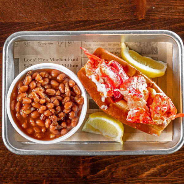 Gaskins Barbecue and Lobster's lobster roll with baked beans and lemon wedges on a metal tray.