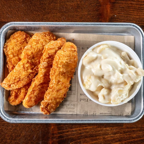 Crispy fried chicken tenders and creamy macaroni and cheese in a metal tray on a wooden table.