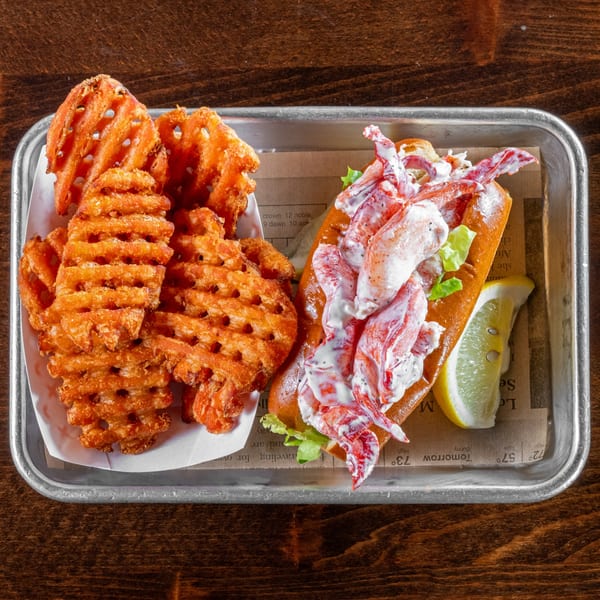 Gaskins Barbecue and Lobster's lobster roll with waffle fries and a lemon wedge on a metal tray.